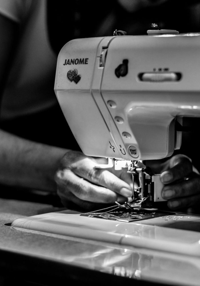 Detailed black and white photo of hands operating a sewing machine, showcasing craftsmanship.
